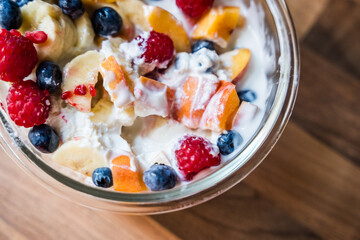 Bowl of fresh fruit salad with yogurt on wooden table surface from top view