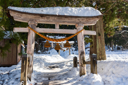 The sacred entrance torii gate of Shirakawa Hachiman Shrine, a peaceful Shinto sanctuary covered in a thick blanket of fresh winter snow. Gifu, Japan