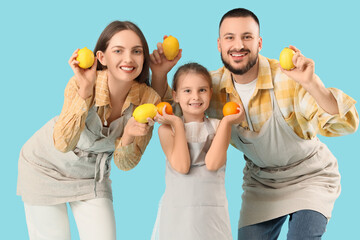 Happy parents with their little daughter in aprons with citruses on blue background