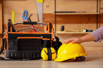 Male hand with hardhat, hearing protectors and tool bag on table in workshop