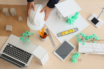 Male architect with hardhat, building model and laptop on table in office