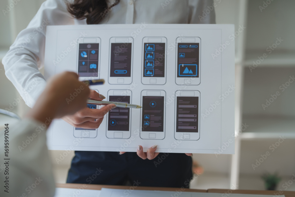 Poster web designers analyzing mobile application wireframes on paper mockup