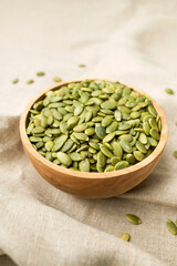Raw peeled green pumpkin seeds in wooden bowl on natural linen fabric background top view. Food...