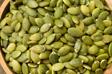 Raw green pumpkin seeds in wooden bowl close up. Food background, organic healthy tasty pumpkin seeds, cooking ingredient top view. Plant-based protein source