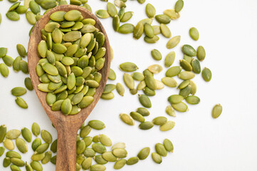 Raw peeled green pumpkin seeds in wooden spoon on light gray white background top view. Food...
