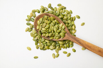 Raw peeled green pumpkin seeds in wooden spoon on light gray white background top view. Food...