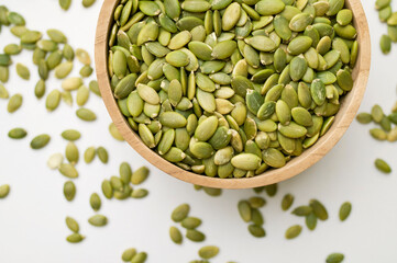 Raw peeled green pumpkin seeds in wooden bowl on light gray background flat lay top view. Food...