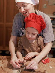 Mother teaching child how to use cookie cutter on gingerbread dough, festive activity. Christmas...