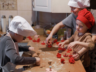 Older child rolls out dough while younger child and mother cut gingerbread cookies, symbolizing...