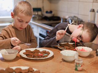 Two boys decorating gingerbread cookies with spoons of icing, holiday family tradition....