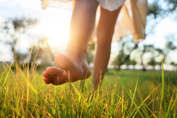 Barefoot young woman walking on green grass in park, closeup
