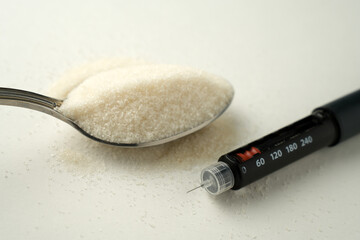 Insulin pen and spoon of sugar on a white background