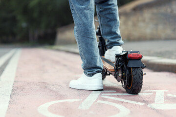 Young man riding electric scooter on bicycle path at city street, closeup