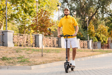 Handsome young man riding electric scooter at city street