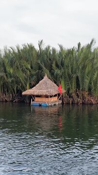 A tranquil river winds through dense mangroves and palm forests beside a remote village in Mataob Maasin, Siargao Islands, Philippines, nestled against green hills under a cloudy sky