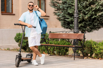 Handsome young man with sunglasses and electric scooter at city street