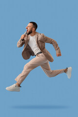 Handsome young man with microphone jumping on blue background