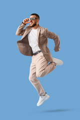 Handsome young man in smart glasses jumping on blue background