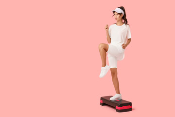 Sporty young woman training on aerobic stepper against pink background