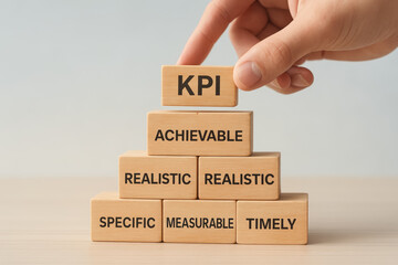 A hand places a block labeled "KPI" atop a pyramid of wooden blocks with key performance indicator terms, emphasizing goal-setting and measurement in business.