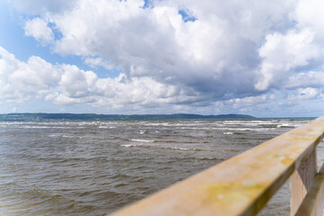 A picturesque wooden pier gracefully extending into the vast ocean beneath a vibrant sky and gentle waves, Bastad, Sweden
