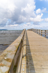 A picturesque wooden pier gracefully extending into the vast ocean beneath a vibrant sky and gentle waves, Bastad, Sweden