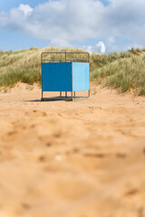 A solitary blue changing room on the beach stands on the beach against the sandy dunes beneath, bright sky above, Sweden