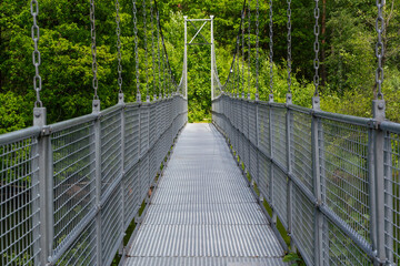 A long and narrow suspension bridge, supported by strong chains, winds its way through vibrant green foliage, Sweden, Knared