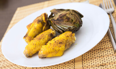 cooked fried chicken wings and halves artichokes on white plate