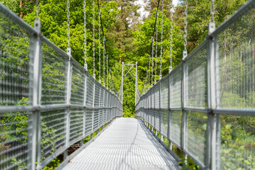 A long and narrow suspension bridge, supported by strong chains, winds its way through vibrant green foliage, Sweden, Knared