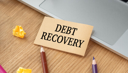 Debt Recovery text on card page with notebook top view on wooden background