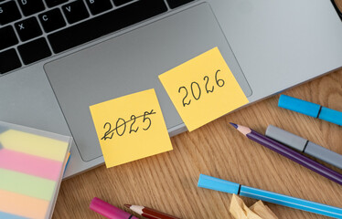Yellow Paper with crossed out inscription 2025 and 2026 on wooden desktop. Planning plans for New...