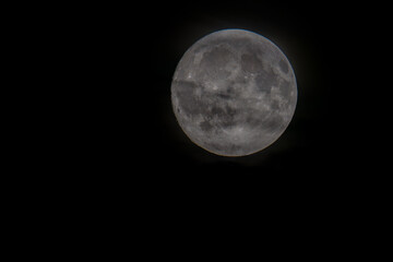 A close-up view of a full moon against a dark sky, showcasing its craters and surface details