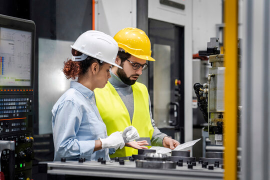 Engineer analyzing blueprint with colleague in factory