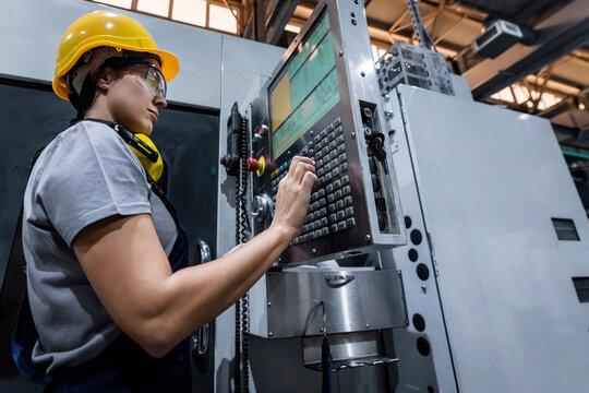 Maintenance engineer wearing hardhat operating CNC machine keypad in modern factory