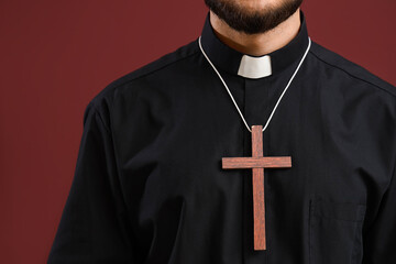 Young priest with wooden cross on red background, closeup