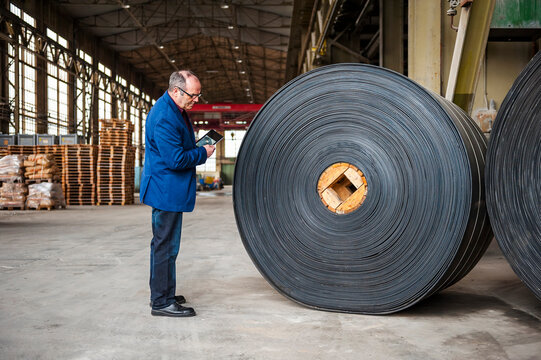 Businessman with tablet inspecting rubber roller in industrial warehouse