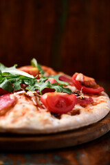 Pizza with salami, tomatoes and mozzarella cheese. Rustic wooden background. Soft focus. Copy space.	