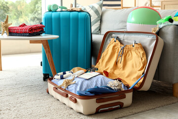 Open suitcase with men's swimwear, passport and beach accessories on floor near sofa, closeup