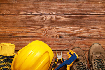 Hardhat, gloves, boots and construction tools on wooden background, top view