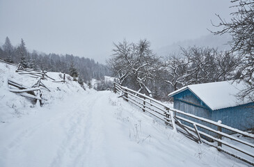 Wooden cabin and fence on a snowy hillside in a mountain valley.