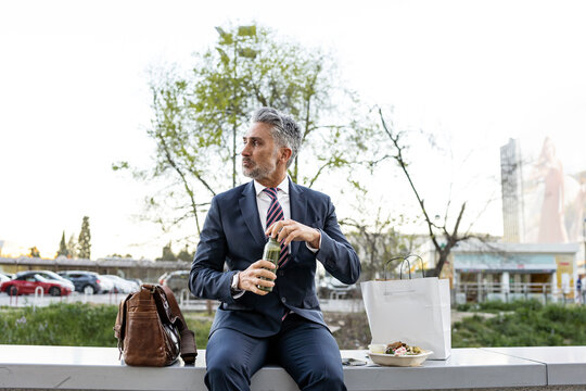 Businessman opening smoothie bottle sitting on wall