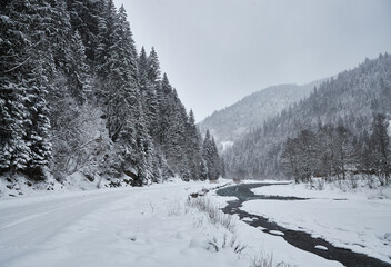 Snowy mountain road alongside a partially frozen river in winter.