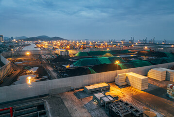 Fototapeta premium Aerial view of a busy commercial cargo port and container terminal with cranes and bright lights at dusk.