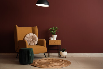 Interior of stylish living room with cozy brown armchair, houseplant and glowing lamp near red wall