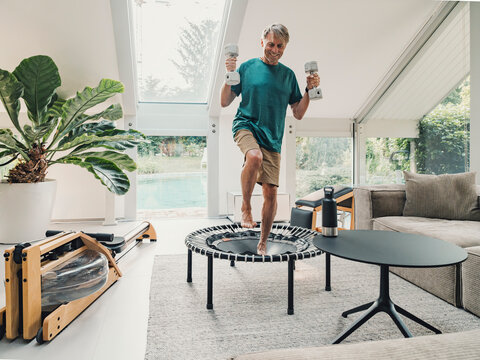 Man exercising with dumbbells on trampoline in a modern living room