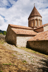 Ancient stone church with tall conical tower standing on hillside under partly cloudy sky, historic...