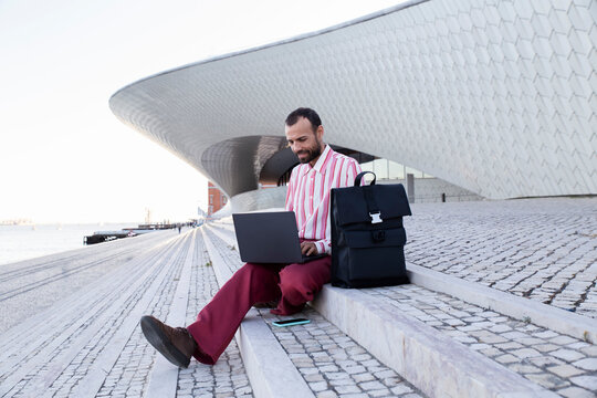 Person working on laptop in red outfit outside Maat Lisbon modern building
