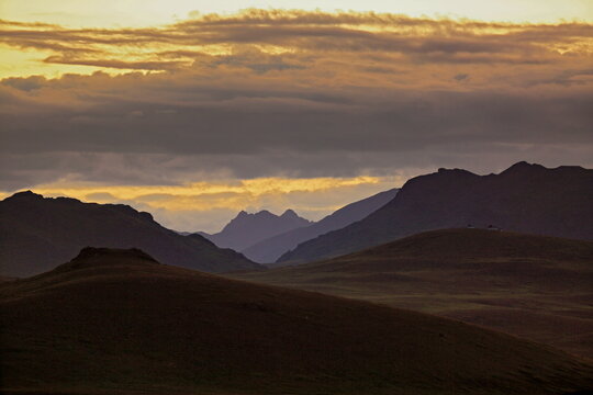 View of the majestic silhouettes of rolling mountains and hills under a tranquil, golden-tinged sky at twilight, Deosai National Park, Gilgit Baltistan, Pakistan.