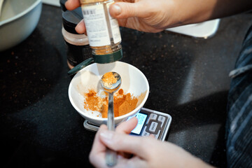Cook hand pours orange spices into cup on kitchen scale placed on kitchen counter